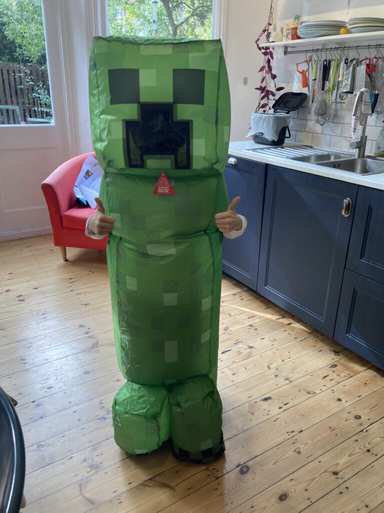 A child wearing a green Minecraft Creeper costume giving two thumbs up